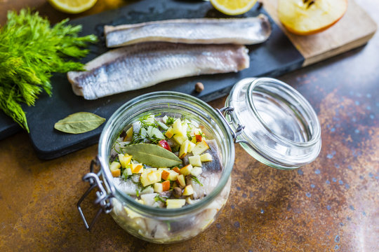 Prepared fresh salted herrings on a stone board and herrings salad in jar.