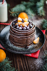 Stack of homemade chocolate pancakes with chocolate topping and tangerines on wooden background