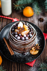 Stack of homemade chocolate pancakes with chocolate topping and tangerines on wooden background