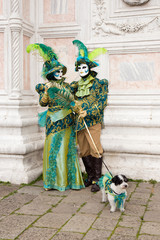 Fototapeta na wymiar Venice Carnival - Lovely Couple of Venetian masks with little dog in colorful and elegant costume San Zaccaria Square - Venice Carnival