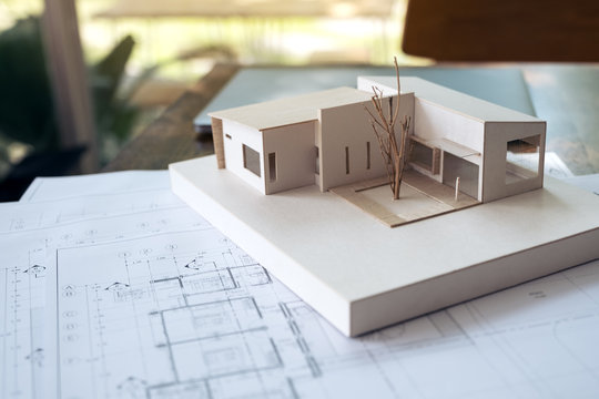 An architecture model with shop drawing paper and laptop on table in office with blur nature background