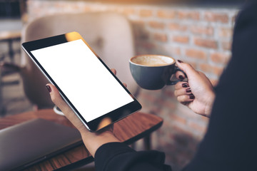 Mockup image of woman's hands holding black tablet pc with blank white desktop screen and coffee cup in cafe background