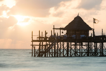 Wooden pier and thatched roofs on a tropical beach at sunrise, Zanzibar island