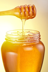 Jar full of fresh honey and honey dipping from wooden spoon into the jar.