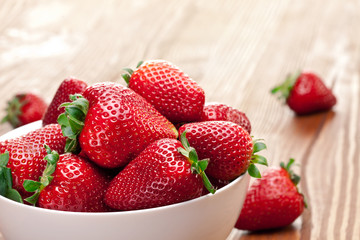 Strawberries in the bowl on wooden table.