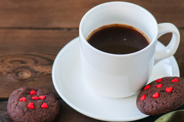 A cup of black coffee and chocolate cookies on a wooden backdrop. Valentine's Day background.