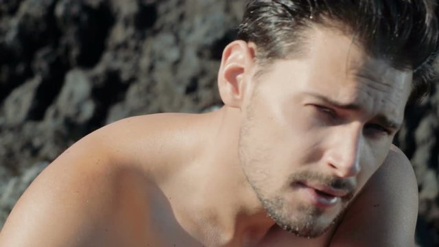 Muscular, handsome man on a tropical, rocky beach - slow motion