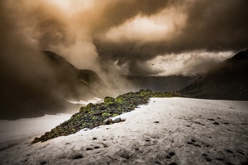 Steinhaufen im Gebirge umgeben von Schnee mit Nebel und Wolken © Oskar