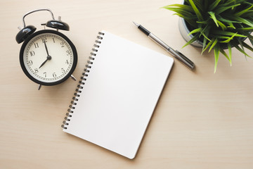 Empty white notebook top view with black alarm clock and pen on wooden table