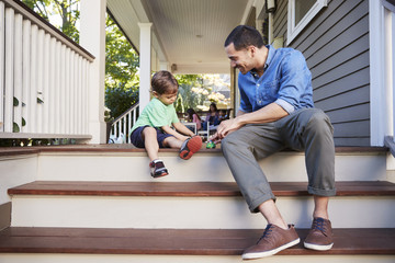 Father And Son Sit On Porch Of House Playing With Toys Together - Powered by Adobe
