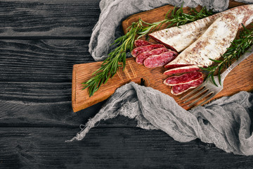 Fuet, Salami and Rosemary. Traditional Spanish sausage. On a black wooden background. Top view.