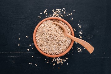 Oatmeal flakes in a plate on a wooden background. Top view. Copy space.