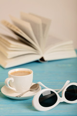 Book, sunglasses and cup of coffee on a wooden blue background.