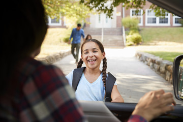 Mother In Car Collecting Daughter In Front Of School Gates