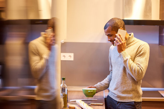A happy handsome young man talking on his phone and cooking in the kitchen.
