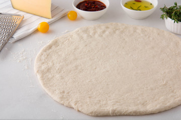 Raw dough for pizza with ingredients.