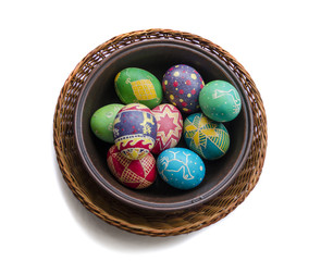 colorful painted Easter eggs in a woven straw basket isolated on white background