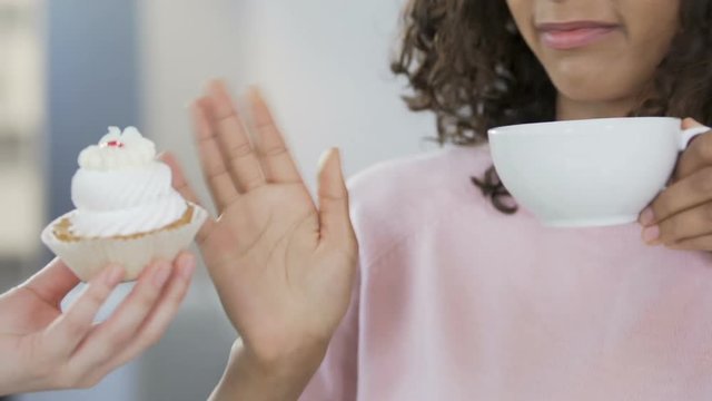 Biracial girl drinking tea and refusing sweet cake, dieting and healthcare