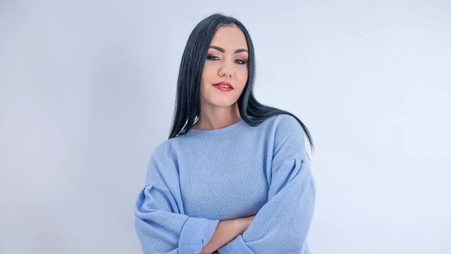 A young woman poses in front of camera. She licks her upper lip and her arms are crossed.