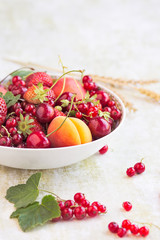 Scodella con frutta estiva su sfondo chiaro: ciliegie, fragole, albicocche e frutti rossi