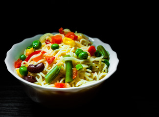 Instant noodles with mixed vegetables in the bowl on dark wooden background with copy space.
