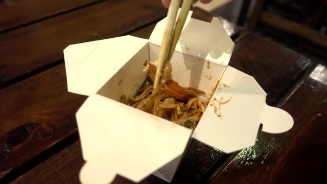 Man eating Chinese Noodles with Chicken and Vegetables with Сhopsticks