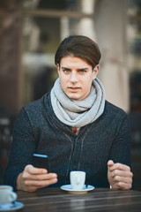 Man using smart phone and drinking coffee while sitting at cafe.