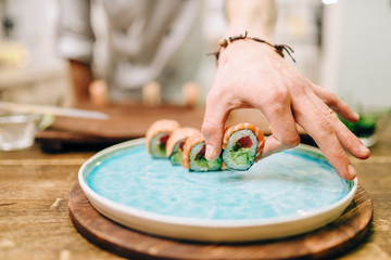 Male person cooking sushi rolls on wooden table
