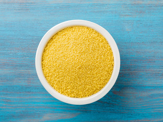 White bowl  with raw couscous on blue wooden background, top view. Traditional Moroccan food