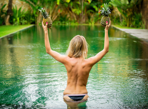 Topless woman dancing with pineapples in the pool
