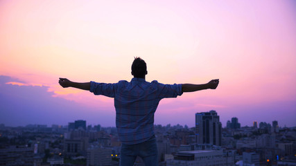 Man stretching hands on roof edge, enjoying freedom, believe in future success - obrazy, fototapety, plakaty