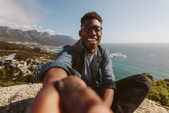 Smiling African Guy On Top Of A Mountain Taking Selfie