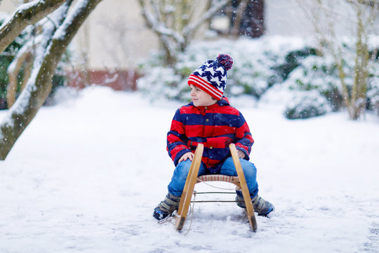 Little kid boy having fung with sleigh ride in winter