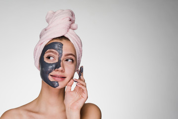 a nice girl with a pink towel on her head applied a clay mask to half of her face, looks away...