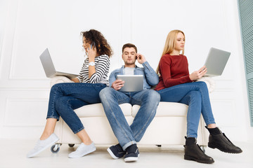 Our workplace. Handsome male person holding tablet in right hand and crossing legs while sitting between his colleagues