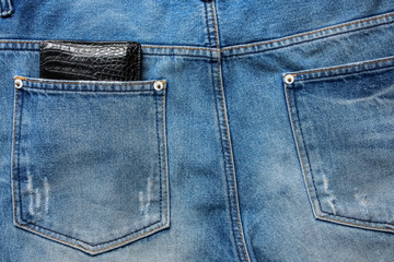 Fototapeta premium Black leather wallet in back blue jeans pocket denim background texture.