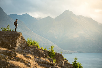 Young Asian male traveler standing on the edge of vista lookout with mountain scenery and Lake...