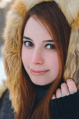 Fashionable beautiful, smile red-haired girl in a snowy forest in a fur coat with fur. Portrait of a brown-haired girl. Winter, snow Women's fashion portrait.