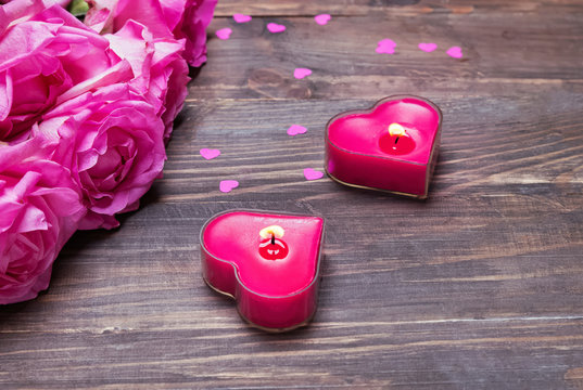 Pink roses and two heart shaped candles on the wooden background