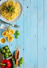Pasta tagliatelle with pesto sauce and other vegetables on a wood background. Top view
