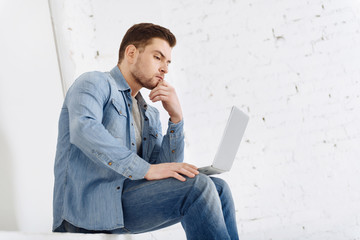 Taking decision. Handsome man raising eyebrows and pressing lips while looking at computer