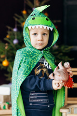 Little child in a green dragon cape stands before a Christmas tree
