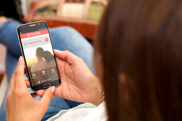 One young woman in her home resting in armchair holding a smartphone with mobile banking  application on the screen.