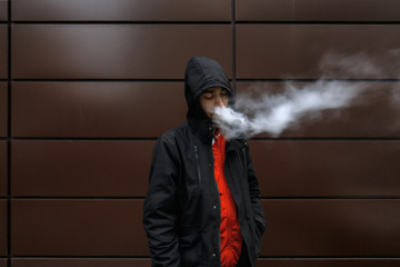 Vape man. Portrait of a bearded handsome young white guy in the hood vaping an electronic cigarette...