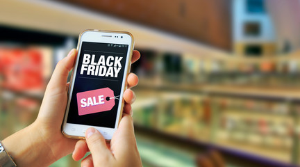 Black Friday. Girl in a Shopping Mall holding a smartphone with a Black Friday advertising on the...