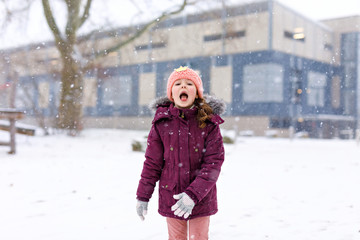 Adorable little kid girl in colorful clothes playing outdoors during snowfall