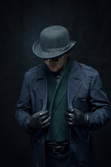 The killer in gloves puts on a raincoat on a black background
