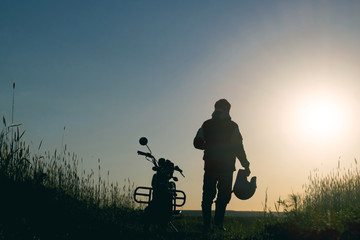 Fototapeta na wymiar The guy near the motorcycle meets the dawn