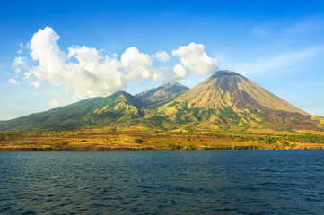 Indonesia landscape. Far island with volcanos and tropical forests among a sea. View from the water.
