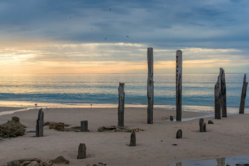 Old jetty pylons on a beach with sunset sky